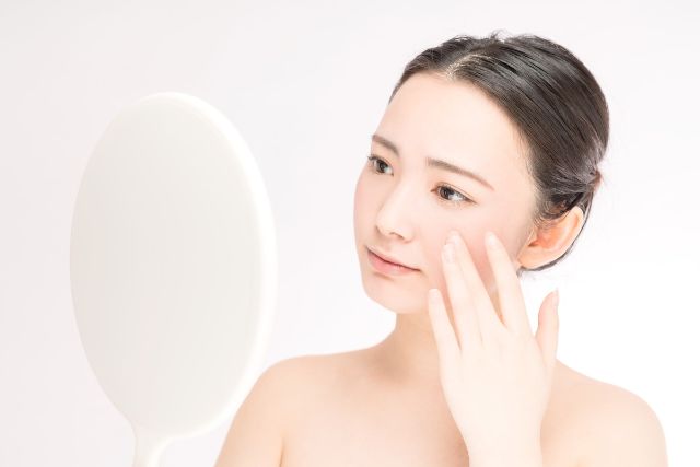 鏡で頬の毛穴を確認する女性